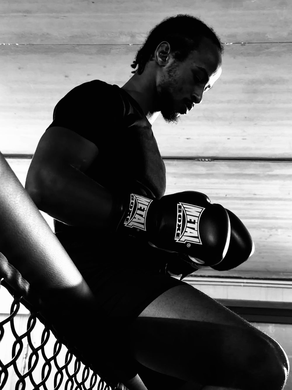 A gloved boxer sitting against the cage after the effort